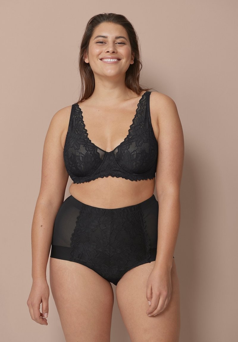 Schwarzer Spitzen-Bralette mit V-Ausschnitt und gewellten Kanten, kombiniert mit hochgeschnittenen schwarzen Panties aus floraler Spitze und durchsichtigen Einsätzen.