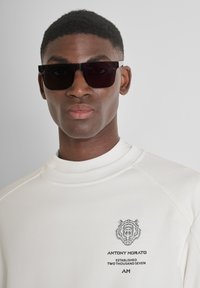 Gafas de sol rectangulares negras, sudadera blanca de cuello alto con gráfico de león negro y texto, textura suave, diseño moderno.