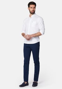 Biała koszula z długim rękawem z kieszonką na piersi, zestawiona z ciemnoniebieskimi spodniami slim fit. Buty w kolorze granatowym, płaskie, o teksturowanym wykończeniu.