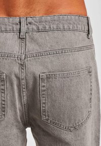 Grijze denim jeans met een klassiek vijf-pocket ontwerp en dikke stiksels. Heeft een middenhoge taille en achterzakken met afgeronde randen.