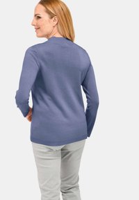 Pull en tricot violet clair à manches longues, avec un ourlet côtelé et une texture lisse, associé à un pantalon gris clair, vu de dos.