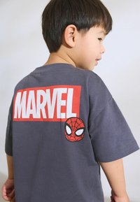 Szürke pamut póló, amelyen élénk piros "MARVEL" felirat található a hátán, és egy Pókember logó a mandzsettán. Rövid ujjú, kerek nyakú kialakítás.