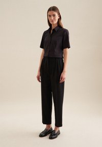 Camicetta nera a maniche corte con bottoni, abbinata a pantaloni neri a vita alta e mocassini neri. Tessuto liscio con una vestibilità comoda.