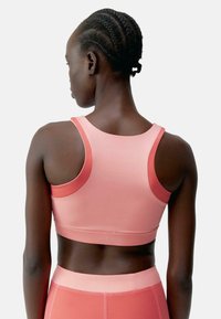 Rózsaszín sportmelltartó sima textúrával, kontrasztos sötét rózsaszín díszítéssel és versenyhát kialakítással. Puha anyag az kényelem és támogatás érdekében.