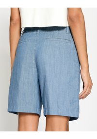 Světle modré denimové šortky s volným střihem, s plochým pasem, dvěma zadními kapsami a lemem sahajícím do poloviny stehno.