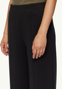 Schwarze weit geschnittene Hose mit einem strukturierten elastischen Bund, ausgestattet mit seitlichen Taschen und einer glatten Stoffoberfläche für Komfort und Bewegungsfreiheit.