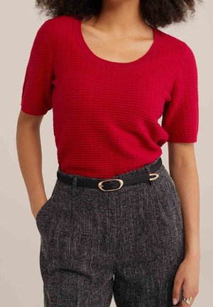 Haut court à manches courtes texturé rouge avec un col rond, associé à un pantalon gris texturé taille haute et une ceinture noire avec une boucle dorée.