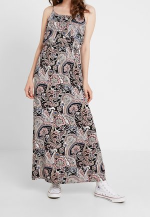 Maxi-jurk in een zwart, roze en crème paisleypatroon. Heeft spaghettibandjes en een getailleerde taille. Gecombineerd met witte sneakers.