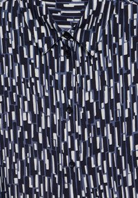 Camicetta a maniche corte con un motivo geometrico blu e bianco, caratterizzata da una base blu scura, chiusura a bottoni e piccoli bottoni neri.
