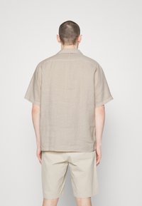 Lichtbeige overhemd met korte mouwen van linnen, voorzien van een standaardkraag, rugpas en een ontspannen pasvorm, gecombineerd met lichtbeige shorts.