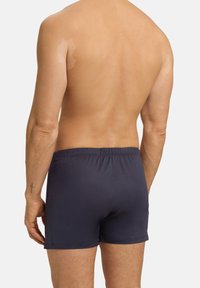 Námořnické modré trenýrky s elastickým pasem, hladkým povrchem a bez viditelných vzorů. Pozadí je neutrální a nevtíravé.