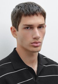 Černé polo tričko s bílými vodorovnými pruhy, s límečkem a krátkými rukávy. Detaily na obličeji a krku mužského modelu.