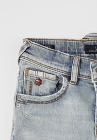 Jeans in denim azzurro chiaro con un classico design a cinque tasche, chiusura con zip frontale e bottone, dettagli cuciti e effetti di usura.