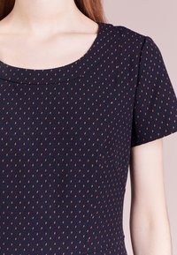 Vestido de marine con mangas cortas y escote redondeado, que presenta una tela texturizada con pequeños patrones naranjas contrastantes en toda su superficie.