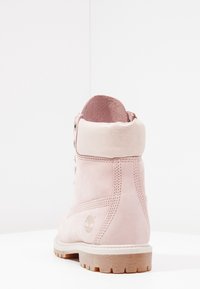 Bottine rose clair avec col rembourré, détails cousus et semelle robuste, présentée de dos sur une surface et un fond blancs.