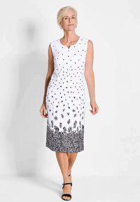 Weißes ärmelloses Kleid mit schwarzem Blumendruck am Saum und kleinen schwarzen Punkten, die im oberen Bereich verteilt sind.