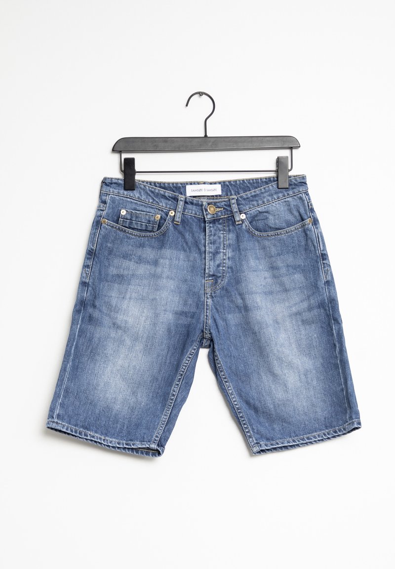 Short en denim bleu avec poches avant et poche monnaie suspendu sur un cintre en plastique noir sur fond blanc uni.