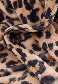 Coperta decorativa con stampa leopardata in tessuto morbido e peluche, con macchie alternate color sabbia e marrone scuro. Presenta bordi arricciati e una texture liscia.