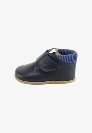 Botas de cuero azul marino con un cuello de ribete azul, correa de velcro y suela de goma color beige. Diseño minimalista con un acabado suave y sin patrones.