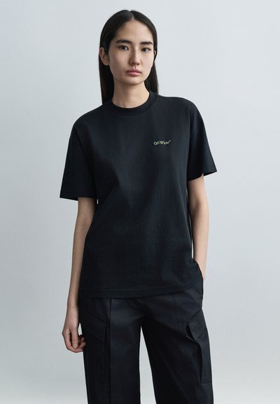 Μαύρο βαμβακερό t-shirt με κοντά μανίκια και στρογγυλή λαιμόκοψη, με πράσινο κεντημένο λογότυπο "Off-White". Φορεμένο με αντίστοιχο μαύρο παντελόνι.