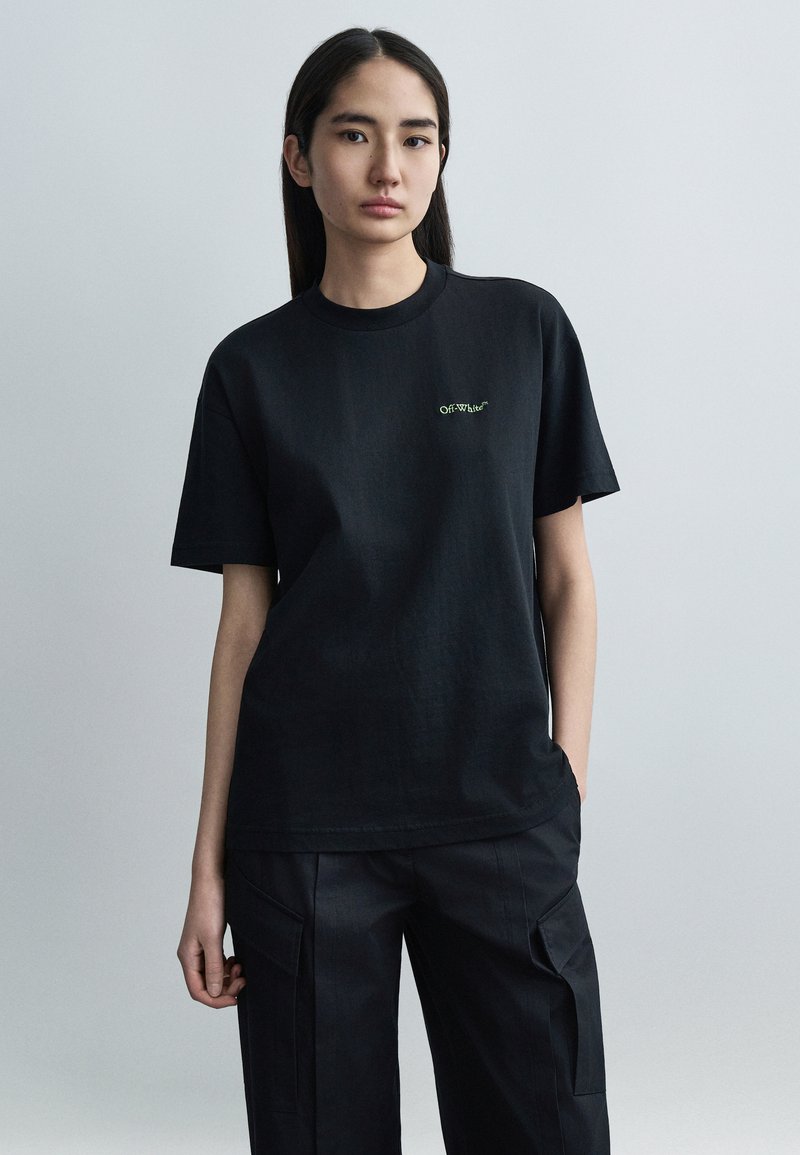 Μαύρο βαμβακερό t-shirt με κοντά μανίκια και στρογγυλή λαιμόκοψη, με πράσινο κεντημένο λογότυπο "Off-White". Φορεμένο με αντίστοιχο μαύρο παντελόνι.