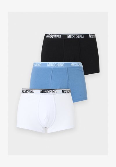 Τρία ανδρικά μποξεράκια σε μαύρο, μπλε και λευκό, το καθένα με ζωγραφισμένη μέση "Moschino", στοιβαγμένα κάθετα σε ανοιχτό φόντο.
