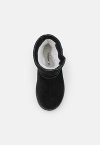 Botte de cheville noire en suède avec une douce doublure en fausse fourrure blanche et un bout arrondi. Dotée d'une semelle flexible et d'un bord supérieur repliant.