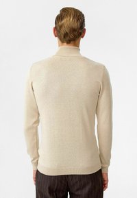 Beige, langemmouwen trui met een hoge kraag en ribbelmanchetten, gemaakt van een soepele, lichte breistekst.