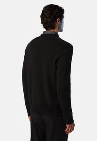 Maglione nero lavorato a maglia con colletto alto, polsini e orlo a coste. Presenta costine verticali lungo le spalle e le braccia superiori.