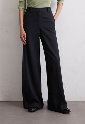 Schwarze weite Hose mit glatter Textur und tailliertem Design, mit flachem Bund, Seitentaschen und kombiniert mit schwarzen Schuhen.