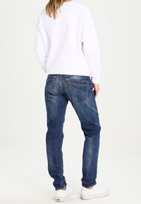 Vit sweatshirt, blå denimjeans, avslappnad passform, enkel bakvy, mjuk textur, minimalistisk design, slitningar på jeansen, vita sneakers.