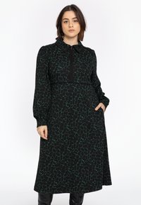 Robe noire longue avec un motif abstrait vert, col boutonné, manches longues et poches latérales. Tissu doux avec une coupe décontractée.