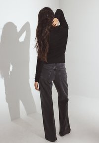 Zwarte langemouwen top in combinatie met donkergrijze wijde jeans. De top heeft een aansluitend ontwerp, terwijl de jeans twee achterzakken heeft.
