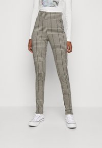 Pantalones de tiro alto y ajustados en un patrón de tejido houndstooth en blanco y negro, con una textura suave y un diseño de pierna estrecha, combinados con zapatillas blancas.