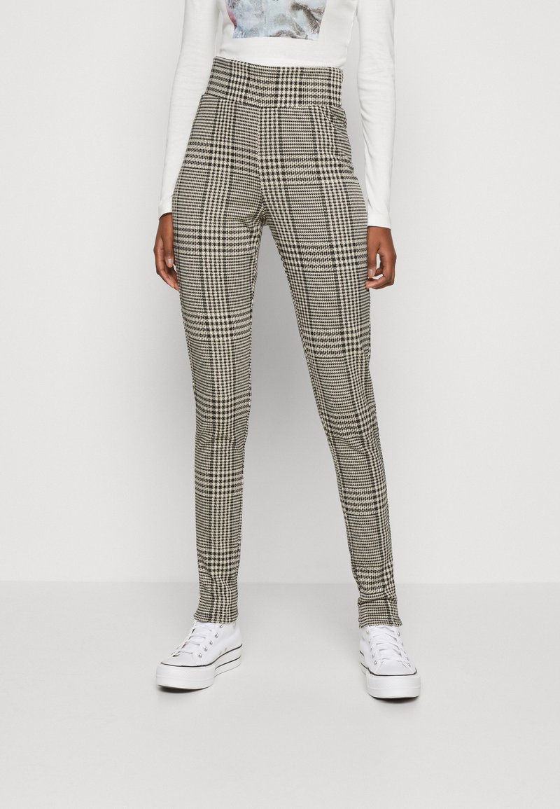 Pantalones de tiro alto y ajustados en un patrón de tejido houndstooth en blanco y negro, con una textura suave y un diseño de pierna estrecha, combinados con zapatillas blancas.
