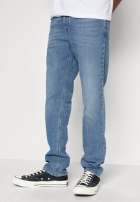 Jeans de denim azul claro con un corte recto. Presentan un diseño clásico de cinco bolsillos y un sutil desgaste. Combinados con zapatillas negras.