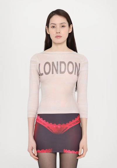 Top transparente de manga larga con "LONDRES" en texto negro en negrita, combinado con una falda ajustada que presenta un estampado gráfico de encaje rojo sobre un tejido oscuro.