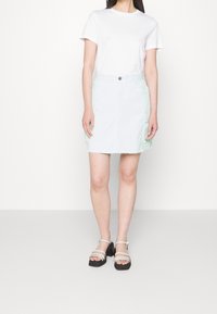 White cotton t-shirt paired with a light denim skirt featuring side pockets and frayed hem. Worn with black block-heeled sandals.