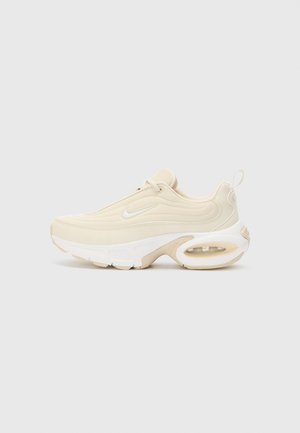 Beige athletic shoe with a smooth texture, slight curves, a padded collar, and a visible air cushioning unit. White sole and subtle branding detail.