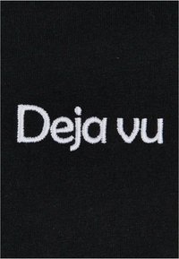Juodas audinys su balta siuvinėta užrašu "Deja vu." Paprastas, švarus dizainas be papildomų raštų ar akcentų.
