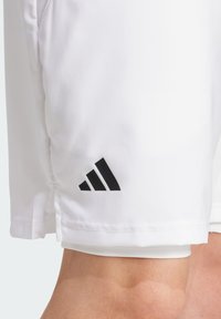 Valged sportlikud lühikesed püksid, mis on valmistatud siledast kangast, millel on must Adidas logo helkuri lähedal. Disain sisaldab külgsuunde liikuvuse tagamiseks.