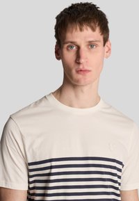 Korte mouw t-shirt in crème met marineblauwe horizontale strepen. Ronde halslijn, zachte katoenstof en klein logo op de borst.