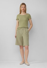 Licht olijfgroene gebreide top met korte mouwen en gegolfde randen, gecombineerd met bijpassende op maat gemaakte shorts. Gedragen met beige geweven ballerina's.