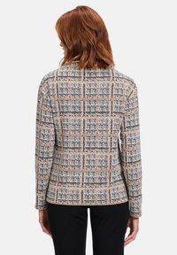Textured blazer in beige, zwart en roestkleur met een ruitpatroon. Heeft een gesneden kraag en een getailleerde pasvorm, gestyled met zwarte broeken.