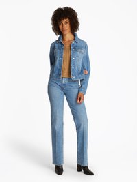 Jaqueta de ganga em azul claro com fechos de botão, bolsos com pala e um colarinho clássico. Combinada com jeans ajustados e botas pretas de salto.