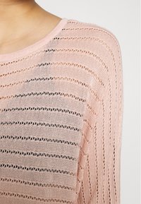 Maglione rosa lavorato a maglia con strisce orizzontali, caratterizzato da sezioni a trame aperte e un ampio collo a giro. Tessuto morbido e testurizzato.