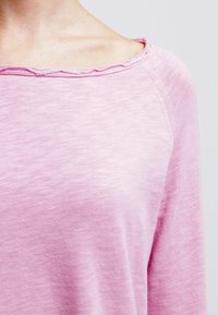 Rosa bomullstopp med en avslappnad passform, med en bred halsringning med råa kanter och en lätt texturerad yta.