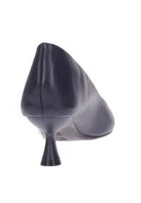 Zapato de mujer de cuero negro con un tacón de aguja estrecho y punta afilada, fotografiado desde un ángulo trasero sobre un fondo blanco.