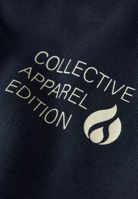 Temno mornarsko modro blago z embosiranim belim besedilom: "COLLECTIVE APPAREL EDITION" z ikono ognja, ki poudarja gladko teksturo in jasen kontrast.