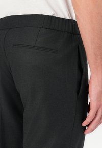 Schwarze Jogginghosen mit einem elastischen Bund, seitlichen Taschen und einer einzelnen Gesäßtasche mit einem dezenten genähten Akzent. Glatte Textur.